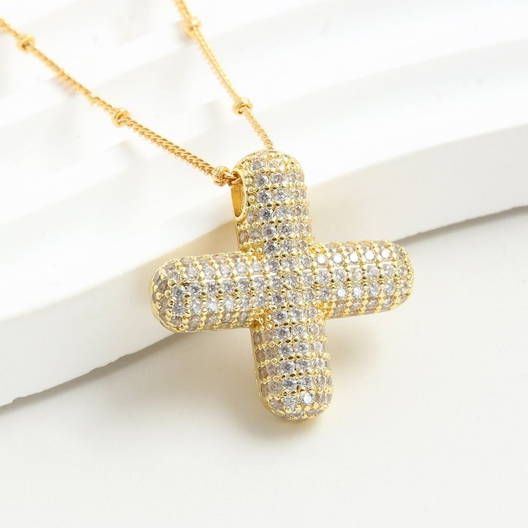 El Collar Inicial Bubble, un collar de oro con un colgante redondeado en forma de cruz con incrustaciones de brillantes diamantes, se muestra sobre un fondo blanco texturado. ¡Lévate 2 por el precio de 1!.