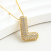 Collar Inicial Bubble - ¡Lévate 2 por el precio de 1! Un collar dorado con dije en forma de letra L y relucientes piedras, elegante sobre fondo blanco. Ideal como regalo personalizado.