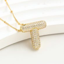 Cargar imagen en el visor de la galería, El Collar Inicial Bubble - ¡Llévate 2 por el precio de 1! destaca con su inicial dorada y diamantes brillantes, siendo un regalo personalizado ideal que resalta sobre un fondo blanco texturizado.
