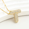 El Collar Inicial Bubble - ¡Llévate 2 por el precio de 1! destaca con su inicial dorada y diamantes brillantes, siendo un regalo personalizado ideal que resalta sobre un fondo blanco texturizado.