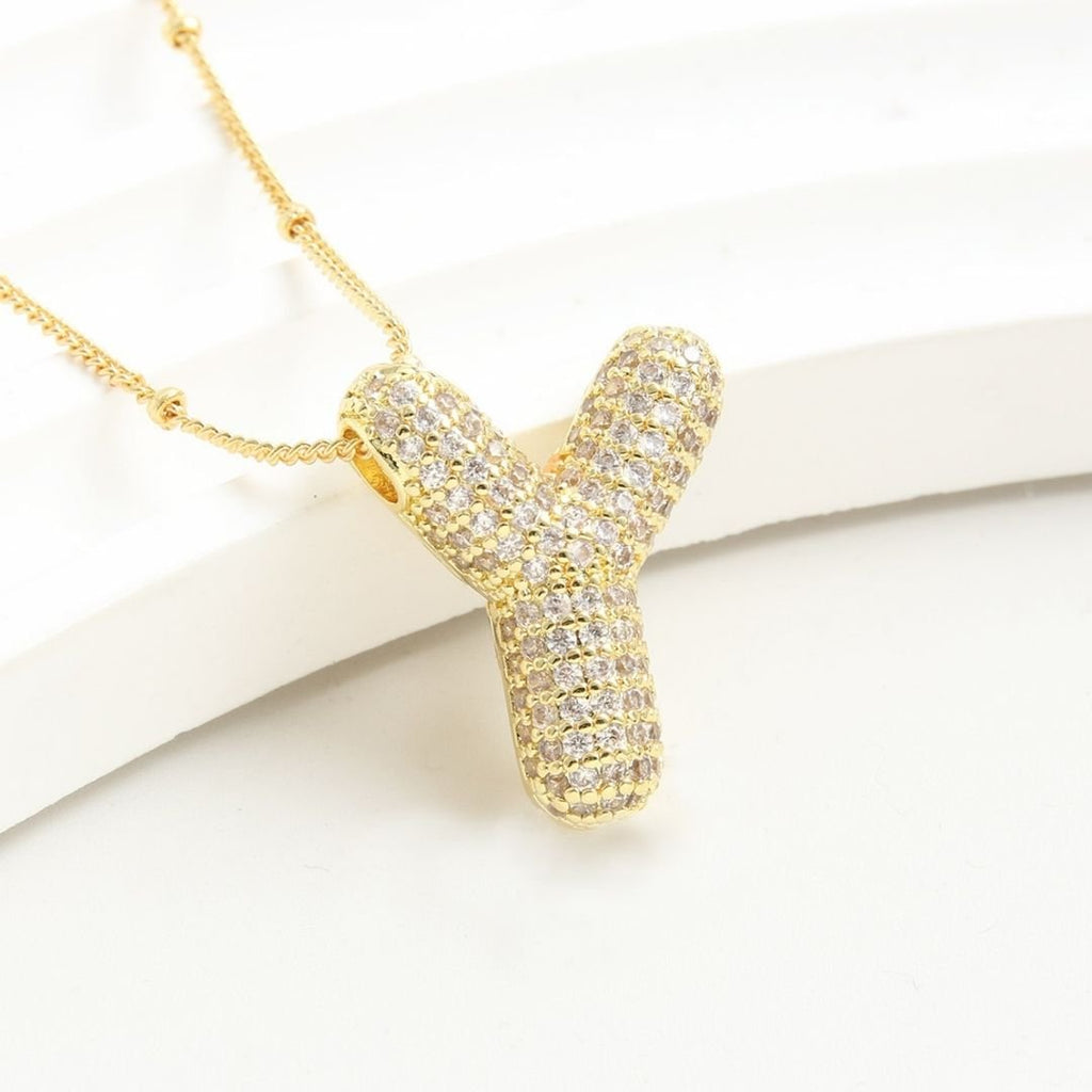 Collar Inicial Bubble - ¡Llévate 2 por el precio de 1! Collar dorado en forma de Y con inicial, incrustado con piedras brillantes, sobre fondo blanco; perfecto como regalo personalizado para cualquier ocasión especial.