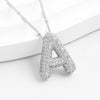 El collar Inicial Bubble - ¡Llévate 2 por el precio de 1! presenta un colgante de plata con forma de letra A, incrustado con piedras brillantes y sobre fondo blanco.