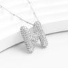 El collar Inicial Bubble, que se muestra en plata con un brillante colgante de una M de strass sobre fondo blanco, es ideal como collar personalizado o regalo personalizado-¡llévate 2 por el precio de 1!.