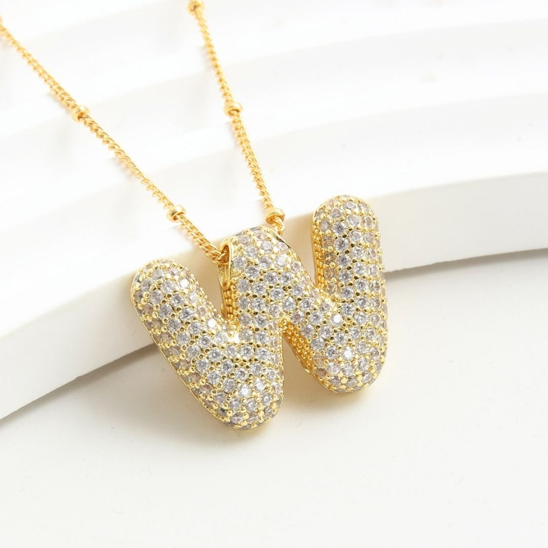 El Collar Inicial Bubble, ¡llévate 2 por el precio de 1!, es un elegante accesorio dorado con iniciales y brillantes piedras claras, ideal como regalo personalizado para cualquier ocasión.