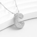 El Collar Inicial Bubble, con dije en forma de C decorado con cristales brillantes sobre fondo blanco, es el regalo personalizado ideal. ¡Llévate 2 por el precio de 1!.