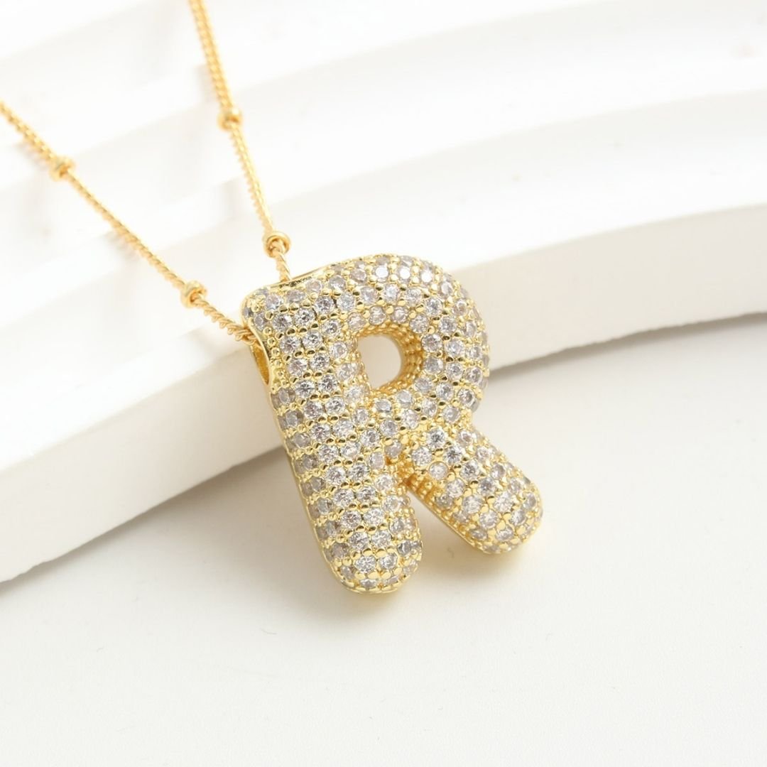 El Collar Inicial Bubble, con colgante R enchapado en oro y diamantes brillantes, se exhibe sobre fondo blanco. ¡Llévate 2 por el precio de 1! Ideal como collar con inicial y regalo personalizado inolvidable.