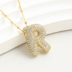 El Collar Inicial Bubble, con colgante R enchapado en oro y diamantes brillantes, se exhibe sobre fondo blanco. ¡Llévate 2 por el precio de 1! Ideal como collar con inicial y regalo personalizado inolvidable.