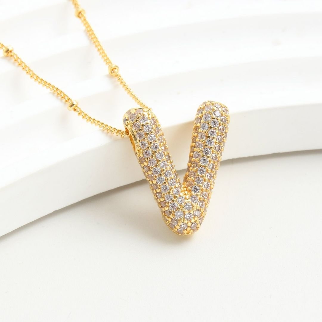 El Collar Inicial Bubble, con dije en forma de V y brillantes piedras claras, se muestra sobre una superficie blanca-¡llévate 2 por el precio de 1! Un regalo personalizado ideal.
