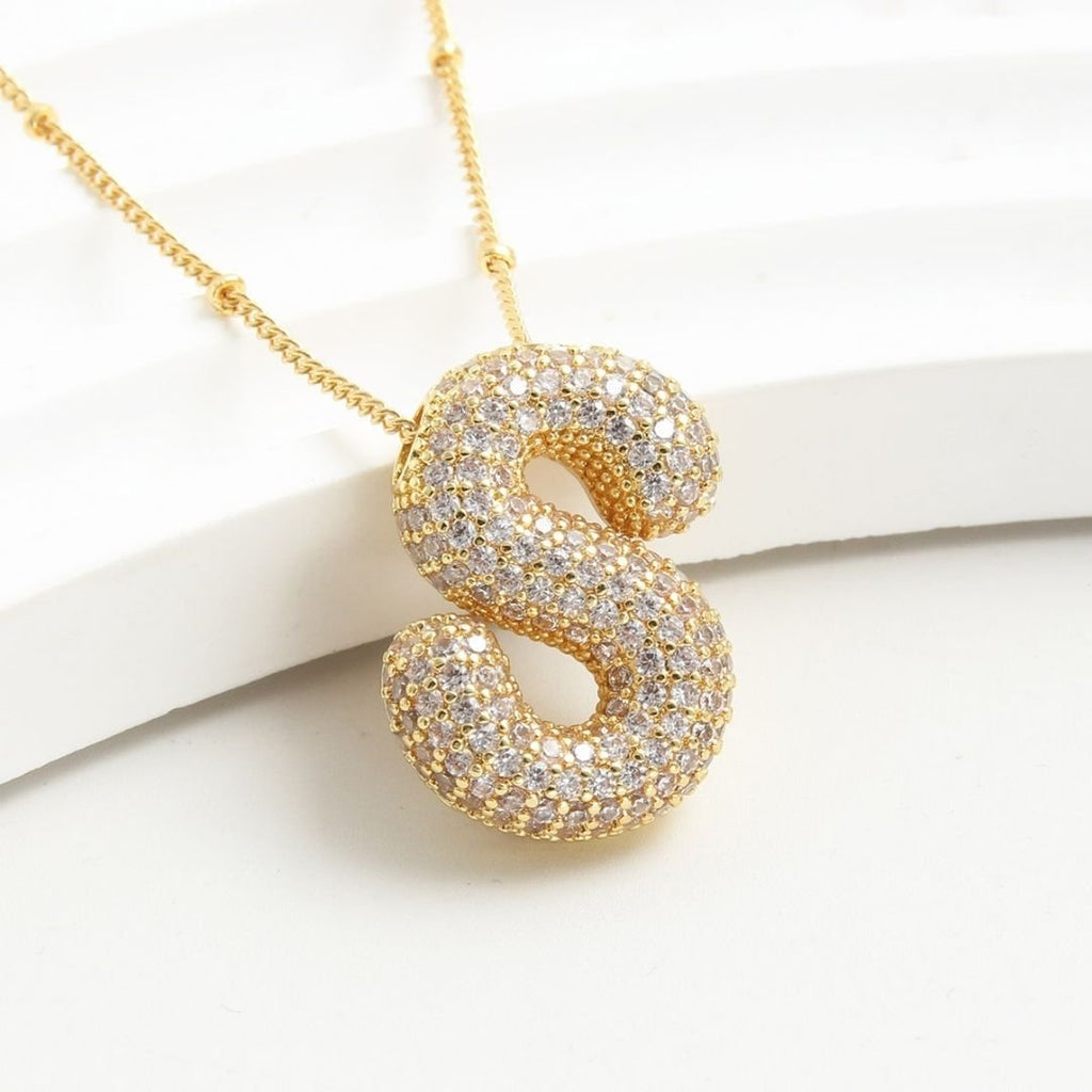 El Collar Inicial Bubble - ¡Llévate 2 por el precio de 1! es un collar personalizado con inicial, decorado con pequeños diamantes, perfecto como regalo especial y presentado sobre fondo blanco.