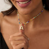 Una mujer sonriente luce el Collar Inicial colorido - ¡Llévate 3 por el precio de 1!, con un gran dije dorado de la letra A, ideal como collar personalizado o regalo para amigas.