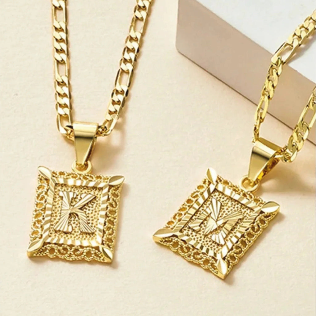 El collar IZAC con inicial personalizada incluye dos collares de oro con gruesas cadenas estampadas y colgantes rectangulares con una inicial K o M en relieve, cada uno de ellos ribeteado con un detalle texturizado que le da un toque especial.