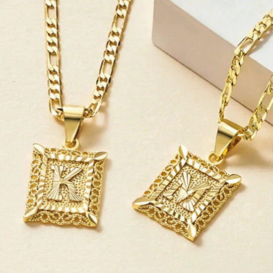 El collar IZAC con inicial personalizada incluye dos collares de oro con gruesas cadenas estampadas y colgantes rectangulares con una inicial K o M en relieve, cada uno de ellos ribeteado con un detalle texturizado que le da un toque especial.