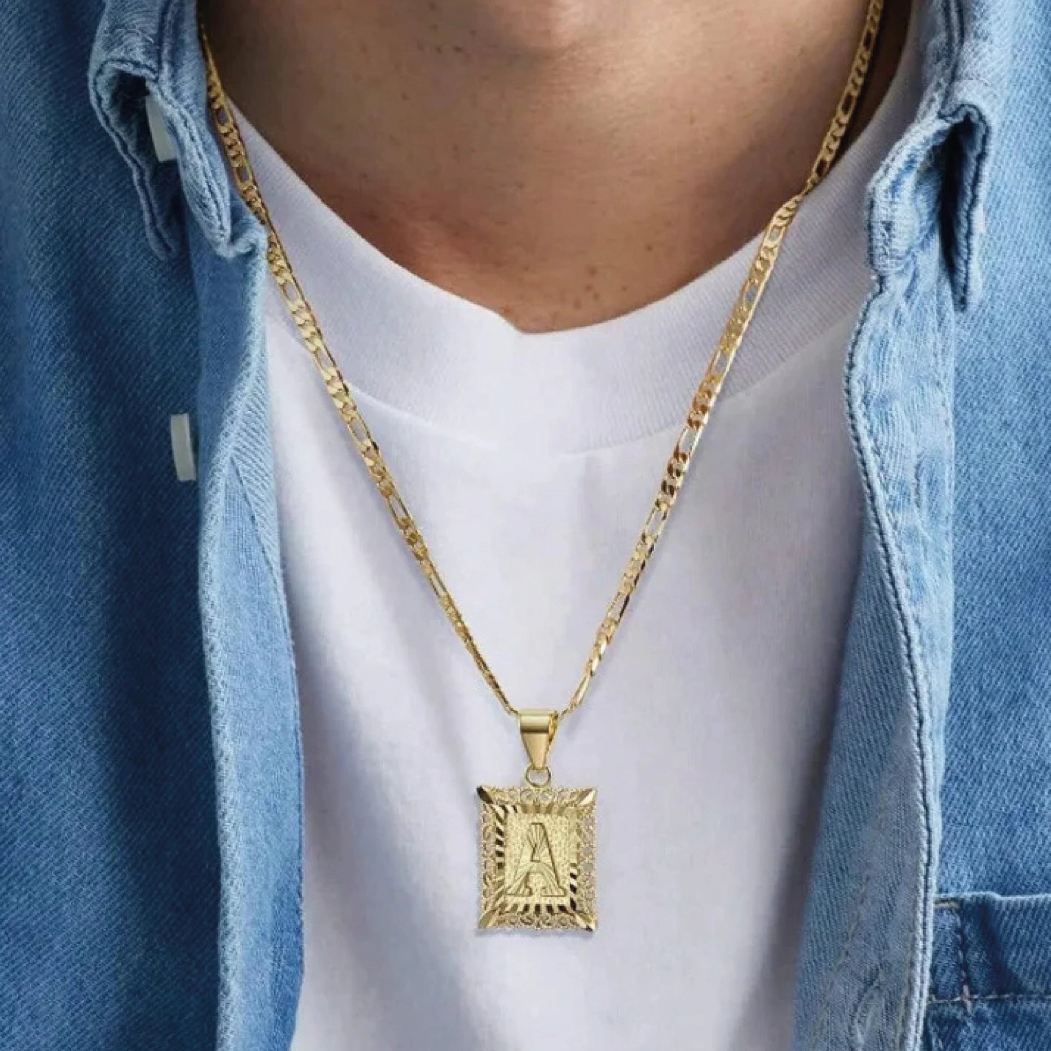 Una persona lleva una camiseta blanca y una camisa de mezclilla azul, con el Collar IZAC con inicial personalizada: un collar elegante de cadena dorada y dije rectangular grabado con la letra A, ideal como collar personalizado.