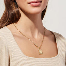 Cargar imagen en el visor de la galería, Una mujer lleva un top de canalé color crema y el collar IZAC con inicial personalizada, que incluye una cadena dorada con un colgante rectangular ornamentado. La foto se centra en sus hombros y destaca el elegante collar personalizado.