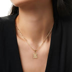 Una mujer con un top negro de cuello en V luce el Collar IZAC con inicial personalizada, un collar de cadena dorada con un colgante rectangular texturizado, una elegante pieza de acero inoxidable perfecta para cualquier atuendo.