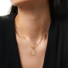 Una mujer con un top negro de cuello en V luce el Collar IZAC con inicial personalizada, un collar de cadena dorada con un colgante rectangular texturizado, una elegante pieza de acero inoxidable perfecta para cualquier atuendo.