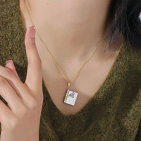 Una persona con un collar dorado "Collar Libro a mi nieta - 'Tú siempre estarás en mi corazón'" con un colgante en forma de libro y una delicada portada, vestida con un top verde texturizado: una joya personalizada y regalo ideal para nieta.