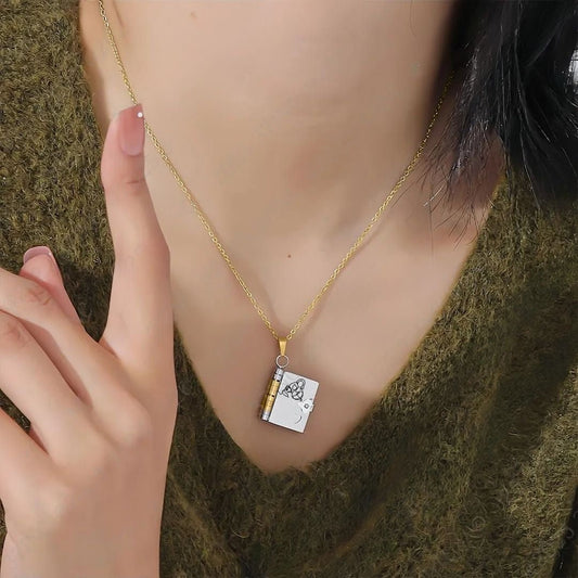 Una persona con un collar dorado "Collar Libro a mi nieta - 'Tú siempre estarás en mi corazón'" con un colgante en forma de libro y una delicada portada, vestida con un top verde texturizado: una joya personalizada y regalo ideal para nieta.