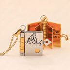 Un medallón dorado y plateado en forma de libro con un corazón recortado, grabado con una madre y su hijo, un regalo ideal: Collar Libro a mi nieta - "Tú siempre estarás en mi corazón"- se abre para revelar páginas doradas y un mensaje personalizado.