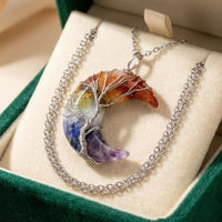 El collar "Luna mística" es un colgante en forma de luna creciente con piedras naturales de colores envueltas en alambre de plata como un Árbol de la Vida, y viene con una cadena de plata a juego en un joyero de terciopelo verde.