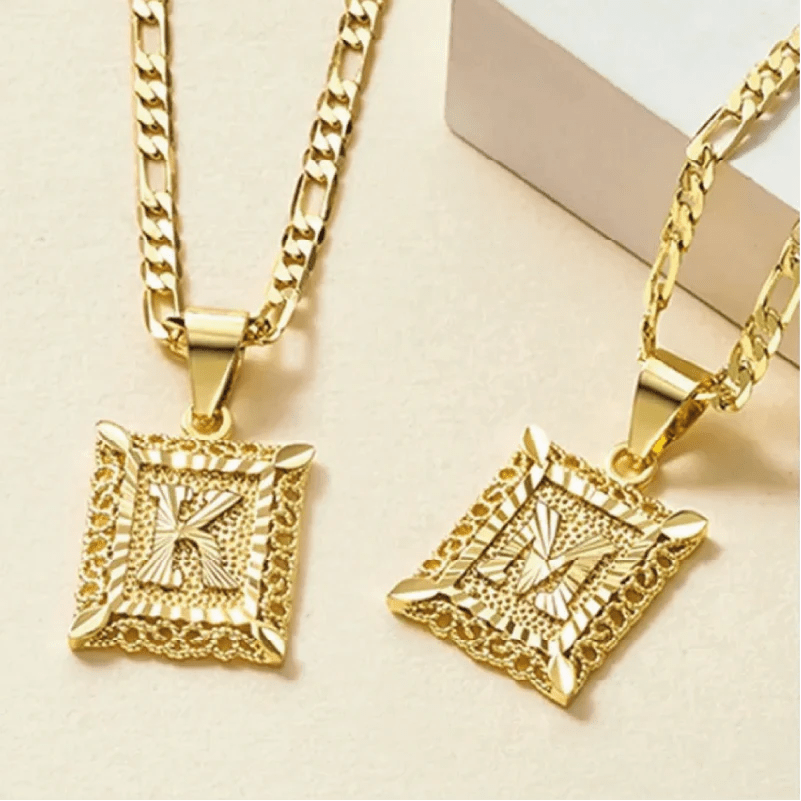 Dos collares Marco con inicial personalizada (Oferta 2x1) de oro con colgantes K y M rectangulares y ornamentados grabados se muestran sobre un fondo claro. Hechos de acero inoxidable duradero, brillan con elegancia para un estilo duradero.