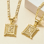 Dos collares Marco con inicial personalizada (Oferta 2x1) de oro con colgantes K y M rectangulares y ornamentados grabados se muestran sobre un fondo claro. Hechos de acero inoxidable duradero, brillan con elegancia para un estilo duradero.
