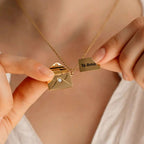 Una persona viste un top blanco y sostiene el collar "Mi carta de amor", un collar de oro con un colgante en forma de sobre que se abre para revelar una pequeña nota de oro grabada con la inscripción "Te Amo", un regalo ideal para su esposa.