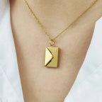 Un primer plano del collar de oro "Mi carta de amor" con un colgante rectangular en forma de sobre, que se lleva en el cuello sobre un top blanco: un regalo ideal para esposa.