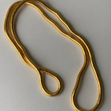 Cargar imagen en el visor de la galería, El Collar moldeable multiuso, una cadena flexible de acero inoxidable de color dorado, se despliega sobre una superficie lisa y clara en bucles sueltos y superpuestos.