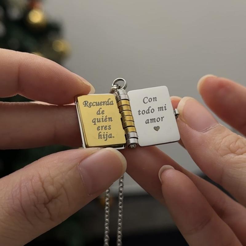 Una persona sostiene un collar para hija "Mi Pequeña Estrella" con un colgante en forma de libro abierto; el lado izquierdo dice "Recuerda de quién eres hija" y el derecho, "Con todo mi amor" junto a un pequeño corazón. Un regalo especial.