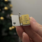 Una mano sostiene el Collar para hija - Mi Pequeña Estrella, un colgante relicario con forma de libro abierto. En uno de los lados tiene un recorte en forma de corazón; en el otro pone "Mi hija increíble" en una placa dorada: un regalo significativo.