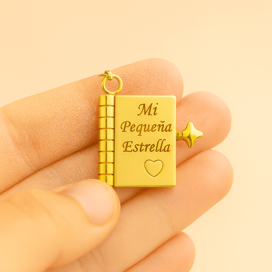 Una mano sostiene el Collar para hija - Mi Pequeña Estrella, un medallón de oro con forma de pequeño libro grabado con "Mi Pequeña Estrella" y un corazón. Este collar de oro incluye una pequeña estrella y una anilla para enganchar a una cadena: un regalo significativo.