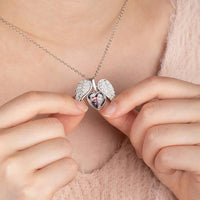 Una persona sostiene un collar personalizado con foto en forma de corazón plateado, abierto para mostrar una pequeña foto de dos personas en su interior. Lleva puesto un top rosa suave y esponjoso.