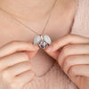 Una persona sostiene un collar personalizado con foto en forma de corazón plateado, abierto para mostrar una pequeña foto de dos personas en su interior. Lleva puesto un top rosa suave y esponjoso.