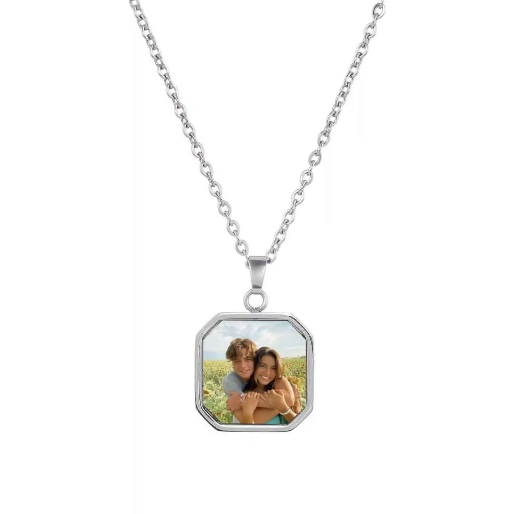 El Collar personalizado con foto secreta, color plateado, captura momentos únicos: dos personas sonriendo y abrazándose al aire libre bajo un cielo azul. Es un regalo personalizado y original.