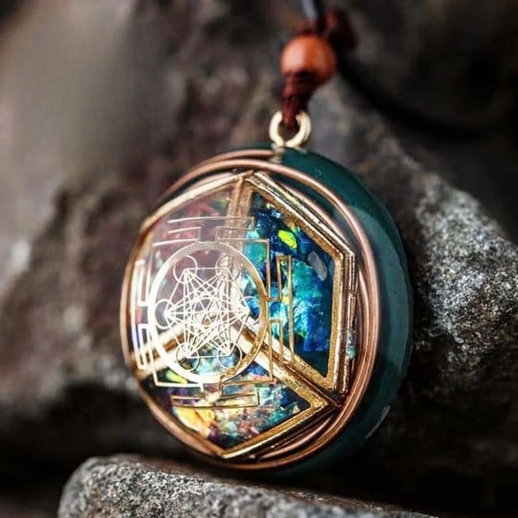 Primer plano del collar Talismán energético con geometría sagrada, con un intrincado alambre de oro sobre un vibrante fondo azul, verde y amarillo iridiscente, diseñado para el bienestar emocional, que descansa sobre piedras grises en bruto.