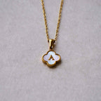 Collar Trébol con inicial: collar de acero inoxidable con dije de concha en forma de trébol, centro blanco y letra A dorada, sobre fondo gris claro. ¡Llévate 2 por el precio de 1!.