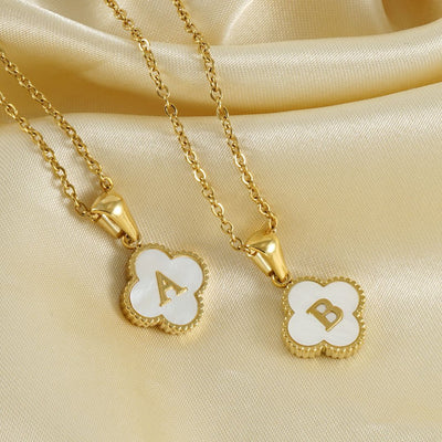 Dos collares trébol con inicial, ambos con dijes de trébol y letras A y B sobre fondo blanco, se exhiben sobre tela satinada dorada. Collar Trébol con inicial - ¡Llévate 2 por el precio de 1!.