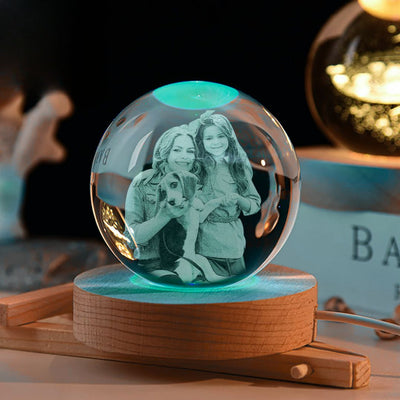 La Esfera de Cristal de los recuerdos muestra una foto grabada en cristal de una mujer sonriente, una niña y un perro, sobre base de madera e iluminada suavemente, creando un ambiente cálido y acogedor.