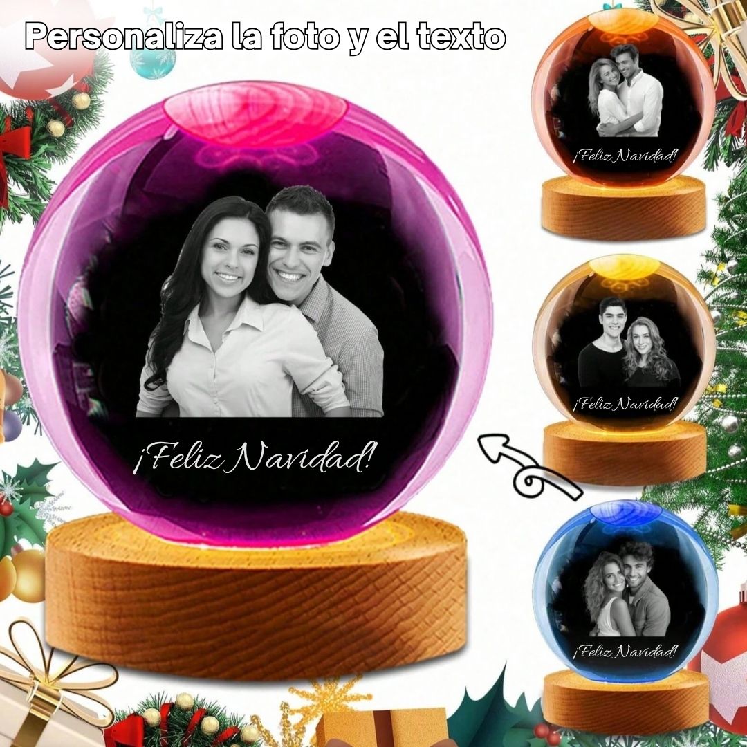 Un festivo anuncio navideño muestra la Esfera de Cristal de los recuerdos con una foto grabada en cristal de parejas sonrientes y el texto ¡Feliz Navidad! La escena incluye adornos, cintas y ramas de pino de fondo.