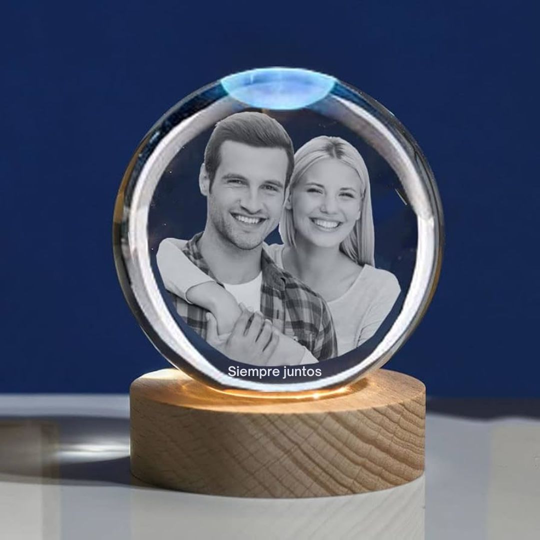 La Esfera de Cristal de los recuerdos con base de madera muestra la foto grabada en blanco y negro de una pareja sonriente y la frase "Siempre juntos" debajo, todo sobre un fondo azul sólido.