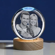 Cargar imagen en el visor de la galería, La Esfera de Cristal de los recuerdos con base de madera muestra la foto grabada en blanco y negro de una pareja sonriente y la frase &quot;Siempre juntos&quot; debajo, todo sobre un fondo azul sólido.