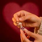 Las manos sostienen un collar Experiencia Perlitta - Ostra real con una perla rosa, sobre un fondo difuminado en forma de corazón que brilla suavemente.