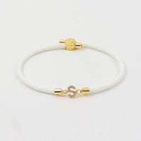 A Pulsera ajustable con inicial (2X1) en color blanco, con extremos metálicos dorados y broche en forma de S decorado con gemas brillantes, exhibida sobre fondo blanco.