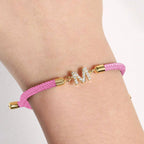 Luce tu estilo único con la Pulsera ajustable con inicial (2X1): banda rosa trenzada, broches dorados y dije M con brillantes. Aprovecha la oferta 2x1 y personaliza tu look con esta pulsera exclusiva.