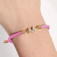 Luce tu estilo único con la Pulsera ajustable con inicial (2X1): banda rosa trenzada, broches dorados y dije M con brillantes. Aprovecha la oferta 2x1 y personaliza tu look con esta pulsera exclusiva.