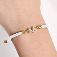 Pulsera ajustable con inicial (2X1) en color blanco, con detalles dorados y charm de letra M decorado con brillantes. Llévala en tu muñeca y aprovecha la oferta 2x1 para lucir esta pulsera personalizada hoy mismo.