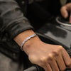 Primer plano de una persona que lleva la Pulsera Alas de ángel, un brazalete de plata y una chaqueta de cuero negro mientras se agarra al manillar de una motocicleta negra.