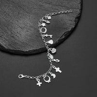 La Pulsera con 13 amuletos (2x1 limitado) incluye corazones, estrellas, una cruz, una llave y una luna creciente en plata 925 sobre una superficie de piedra negra texturizada, ideal para atraer energía positiva a tu vida diaria.
