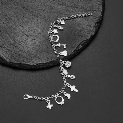 La Pulsera con 13 amuletos (2x1 limitado) incluye corazones, estrellas, una cruz, una llave y una luna creciente en plata 925 sobre una superficie de piedra negra texturizada, ideal para atraer energía positiva a tu vida diaria.